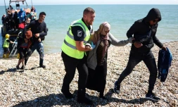 Un officier interforce aide une femme migrante sur la plage de Dungeness, sur la cÎte sud-est de l'Angleterre, le 16 août 2023