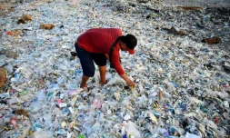 Un homme fouille dans des ordures et déchets plastiques échoués sur la plage de Kedonganan, sur l'ßle indonésienne de Bali, le 19 mars 2024