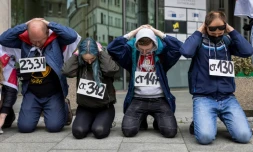 Des militants bélarusses manifestent devant les bureaux de la Commission européenne à Varsovie le 29 mai 2021 en posant comme s'ils étaient arrêtés, avec sur la poitrine la référence d'un article du code pénal invoqué pour l'arrestation du journaliste dissident Roman Protassevitch
