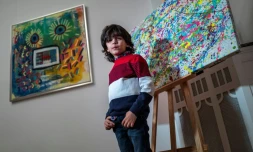 L'artiste allemand de 7 ans Mikail Akar pose devant ses peintures "Champi" (d) et "Homme tournesol" avant l'ouverture de son exposition "Manus 11" à Berlin, le 13 décembre 2019