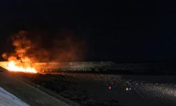 Des policiers éloignent des bidons d'essence d'un canot en feu sur la plage du Portel (Pas-de-Calais) le 21 septembre 2024