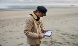 Le "beachcomber" belge Aäron Fabrice de Kisangani regarde un carnet abandonné par des migrants sur la plage de Gravelines, le 26 mars 2025 dans le Nord
