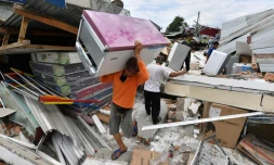 Un homme transporte un réfrigérateur extirpé des ruines d'une boutique le 8 août 2018 à Bangsal, en Indonésie