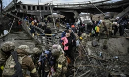 Des habitants évacuent la ville d'Irpin (Ukraine), au nord-ouest de Kiev durant d'intenses bombardements le 5 mars 2022, empruntant les restes d'un pont que la défense ukrainienne avait fait sauté la semaine derniÚre pour ralentir l'avance russe