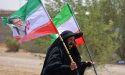 Une pèlerine iranienne brandit des drapeaux iraniens dont l'un comprend un portrait du guide suprême Ali Khamenei, tué dans un bombardement américain, le 29 juillet 2026 dans la ville-frontière de Zurbatiyah, en Irak