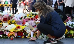Une femme allume une bougie aprÚs avoir déposé des fleurs, le 14 avril 2024, en hommage aux victimes de l'attaque au couteau dans un centre commercial à Sydney