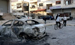 Un jeune fait du vélo à côté d'une voiture détruite après les affrontements entre les nouvelles autorités syriennes et les partisans du président déchu Bachar al-Assad dans la ville de Jableh, dans la province côtière de Lattaquié, le 10 mars 2025