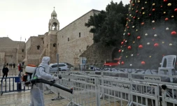 Un employé en combinaison de protection désinfecte les abords de l'église de la Nativité, avant les célébrations de Noël, le 24 décembre 2020 à Bethléem