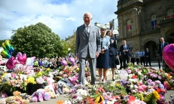 Le roi Charles IIIl s'arrête devant les fleurs déposées devant la mairie, après le meurtre de trois fillettes fin juillet dans une attaque au couteau, lors de sa visite pour rencontrer les membres de la communauté locale, le 20 août 2024 à Southport, au nord-ouest de l'Angleterre