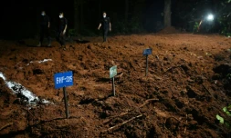 Des agents de police marchent à proximité de tombes de victimes non identifiées de la crue dévastatrice, le 30 août 2026 à Devghat au Népal