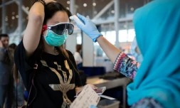 Une hôtesse de l'air de Malaysia Airlines prend la température d'une passagère chinoise à l'embarquement d'un vol pour Pékin, le 14 février 2020 à l'aéroport de Kuala Lumpur