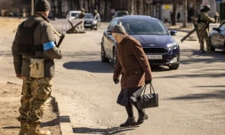 Une femme traverse une chaussée devant des membres des forces ukrainiennes à un point de contrÎle à Kiev, le 21 mars 2022