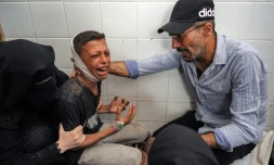 Un homme et une femme réconfortent à la morgue d'un hÎpital de Deir el-Balah dans le centre de Gaza, un garçon blessé qui pleure la perte de son pÚre tué dans un bombardement israélien, le 25 juin 2024