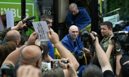 Des prisonniers de guerre ukrainiens libérés enveloppés dans le drapeau national débarquent d'un bus à leur arrivée après un échange de prisonniers dans la région de Tcherniguiv, le 26 juin 2025, en Ukraine