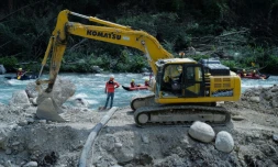 Des touristes en rafting sur la rivière Roya passent près d'un bulldozer reconstruisant une route, dix mois après la tempête Alex, le 12 août 2021 à Breil-sur-Roya, dans les Alpes-Martimes