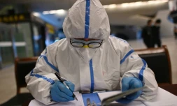 Un employé en combinaison de protection vérifie les documents d'identité des voyageurs arrivant à la gare de Wuhan, dans la province chinoise du Hubei, le 28 mars 2020