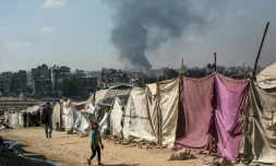 Des Palestiniens devant des tentes à Gaza-ville avec en arrière-plan une colonne de fumée s'élevant du centre de la bande de Gaza après un bombardement israélien, le 6 juillet 2025