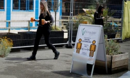 Une femme porte deux biĂšres sur une berge de la Tamise, prĂšs d'une affiche faisant la promotion de la distanciation sociale Ă Londres, le 3 juillet 2020.