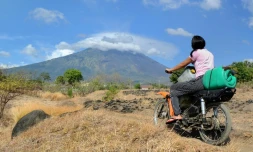 Une femme traverse en moto un paysage dominé par le mont Agung qui menace d'entrer en éruption, ce qui a provoqué l'évacuation de 75.000 habitants, à Bali le 26 septembre 2017