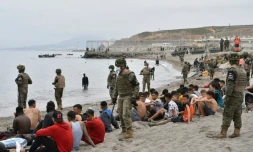 Des migrants, parmi lesquels des mineurs, arrivés à la nage depuis le Maroc sur l'enclave espagnole de Ceuta, se reposent devant des soldats espagnols montant la garde le 18 mai 2021