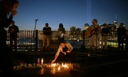 Une femme allume une bougie et une autre joue de la guitare lors d'une veillée interconfessionnelle à Brooklyn Heights avec l'illumination sur le site de Ground Zero en toile de fond, à New York le 11 septembre 2021
