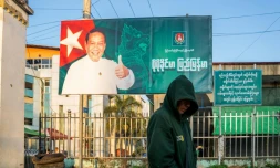 Cette photo prise le 20 décembre 2025 montre un homme passer devant un panneau de campagne de Khin Yi, de l'Union pour la solidarité et le développement, dans la région de Shan en Birmanie