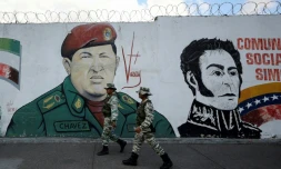 Des miliciens passent devant une fresque murale figurant l'ancien président vénézuélien Hugo Chavez et le libérateur Simon Bolivar, le 7 janvier 2025 à Caracas