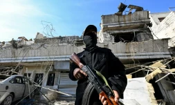 Un membre des forces de sécurité syriennes monte la garde devant un bâtiment détruit par une frappe aérienne israélienne à Damas, le 13 mars 2025