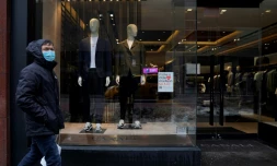 Un homme passe devant la vitrine d'un magasin de vĂȘtements masculins, montrant des mannequins en veste, t-shirt et baskets, sur Madison Avenue, le 15 fĂ©vrier 2021