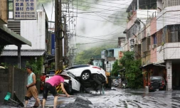 Des habitants nettoient la boue devant chez eux, avec des véhicules renversés en arrière-plan, après la rupture d'une digue au passage du super typhon Ragasa, à Hualien à Taïwan, le 24 septembre 2025