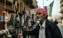 Un passant à proxmité d'échoppes ouvertes dans une rue d'Alep où flotte le drapeau de la rébellion, le 11 décembre 2024.
