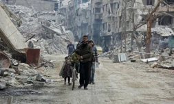 Photo prise le 30 mars 2018 montrant des civils marchant le long de bâtiments détruits à Harasta, une semaine après la reprise de cette ville par le régime