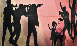 Une femme passe devant une fresque murale représentant des hommes armés visant des manifestants, allusion à la répression policière, dans une avenue de Tegucigalpa, le 27 novembre 2025