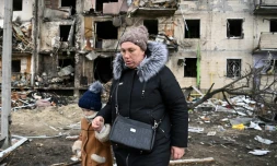 Une femme avec un enfant marche devant un immeuble résidentiel endommagé dans la rue Koshytsa, une banlieue de la de Kiev, le 25 février 2022.