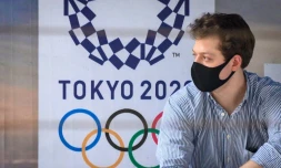 Un homme, portant un masque, à un arrêt de bus devant une affiche des JO-2020, le 16 mars 2020 à Bangkok