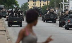 Une femme regarde les soldats ivoiriens qui patrouillent près du quartier général de l'armée, le camp militaire de Gallieni, à Abidjan le 12 mai 2017