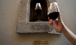 Une personne tient un verre de vin Ă cĂŽtĂ© d'une "fĂȘnĂȘtre Ă vin" dans une rue de Florence, le 12 aoĂ»t 2020 en Italie