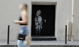 Une femme passe devant le pochoir de l'artiste Bansky le 25 juin 2018, dans une rue près de la salle de concert du Bataclan