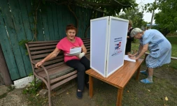 Une femme examine des bulletins de vote dans un bureau de vote mobile installé par les membres d'une commission électorale locale, accompagnés d'un militaire russe, à Novonikolayevka, dans la région de Donetsk, en Ukraine sous contrÎle russe, le 14 septembre 2026