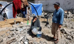 Une femme assise avec des récipients vides devant une tente installée prÚs des décombres d'un immeuble détruit à Rafah dans le sud de la bande de Gaza, le 5 avril 2024