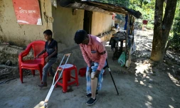 Ali Hossain (à droite), un Bangladais de 40 ans qui a perdu une jambe à cause d’une mine lorsqu'il ramassait du bois, retire sa prothèse devant sa maison dans le district de Bandarban le 19 décembre 2025