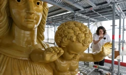 La restauratrice d'art Cyrielle D'Antoni travaille avec des feuilles d'or sur la statue de Jésus, à côté de la Vierge Marie, lors de la rénovation de la basilique Notre-Dame de la Garde à Marseille, le 3 septembre 2025
