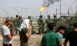 Des jeunes irakiens manifestent devant l'entrée d'un champ pétrolier gardé par des soldats, le 14 juillet 2018 à Al-Qournah, dans la province de Bassora (sud)