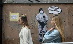 Deux femmes passent devant un message mural où il est écrit: "Il y a une épidémie d'ignorance dans l'air, nous devons nous protéger", par l'artiste Laika, près du quartier chinois de Rome, le 4 février 2020