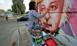 L'artisqte irakienne Wijdan al-Majed apporte quelques touches à une fresque du poète irakien Muzaffar al-Nawab sur un mur de Bagdad, le 26 avril 2022
