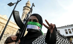 Une femme masquant son visage avec le drapeau de l'opposition syrienne fait le V de la victoire en tenant un fusil d'assaut devant la mosquée des Omeyyades à Damas le 10 décembre 2024