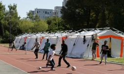 Des migrants jouent au foot devant des tentes installées par la Sécurité civile sur un terrain de sport dépendant de l'Université Panthéon-Assas le 22 août 2017 