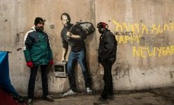 Des migrants devant une oeuvre de l'artiste britannique Bansky photographiée le 12 décembre 2015 et située à l'entrée de la "Jungle" de Calais, représente Steve Jobs (Apple), qui porte un baluchon et un vieil ordinateur