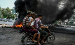 Des hommes à moto passent près d'une barricade en feu, à Rangoun en Birmanie le 17 mars 2021