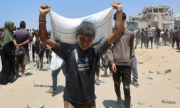 Des personnes se déplacent dans la rue al-Rashid, dans l'ouest de Jabalia, le 22 juillet 2025, après avoir reçu une aide humanitaire dans un centre de distribution situé dans le nord de la bande de Gaza
